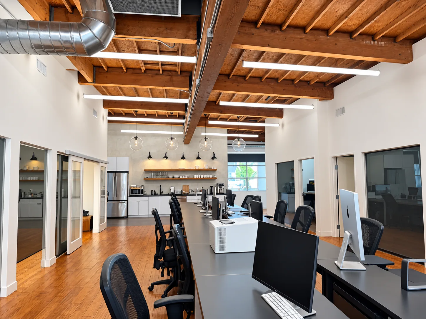 Existing studio with a central worktable, private rooms, exposed timber beams and kitchen