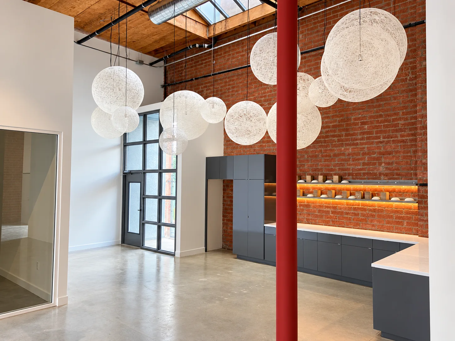 Brick-lined interior with suspended spherical pendants, red column and kitchen cabinetry